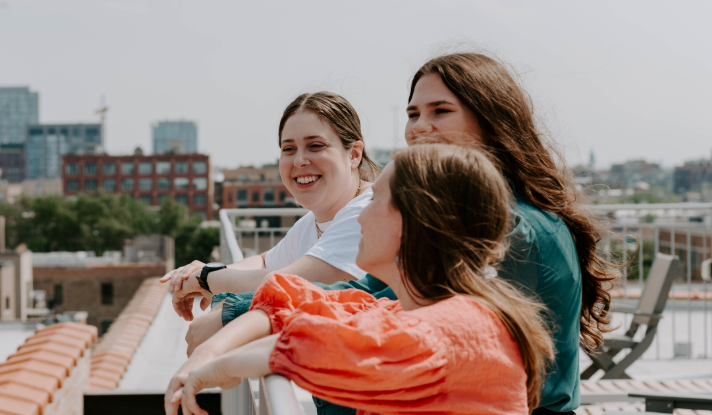 Three female counselors in Chicago standing against a railing on the roof of their therapy office laughing.