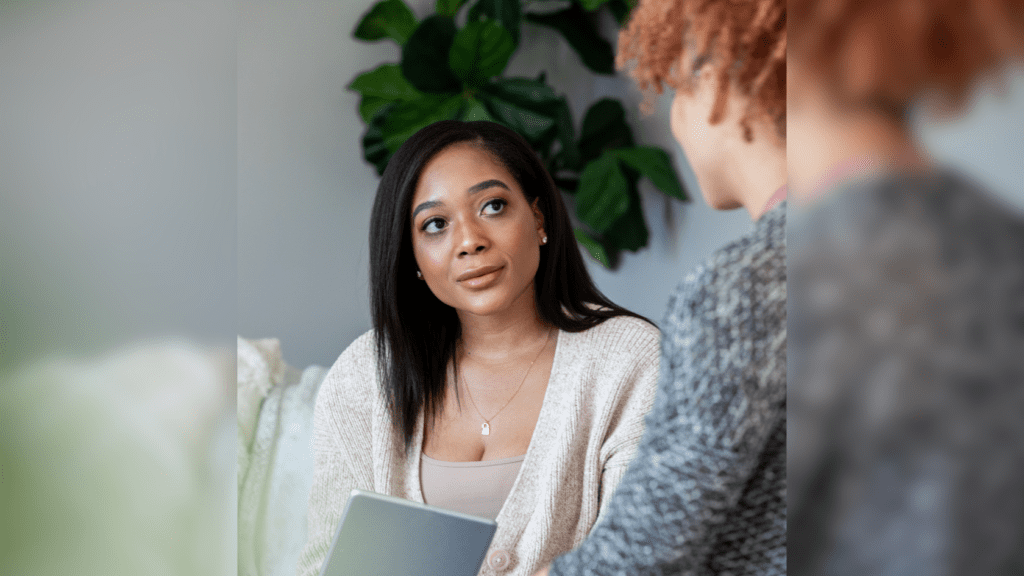 Black woman sitting on a couch listening to another woman.