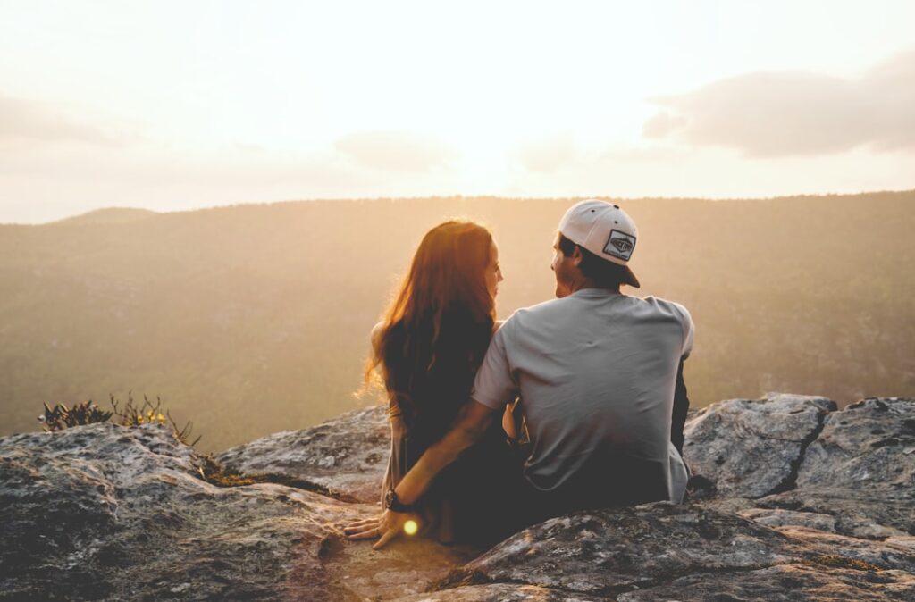 couple sitting on mountain at sunset smiling at eachother