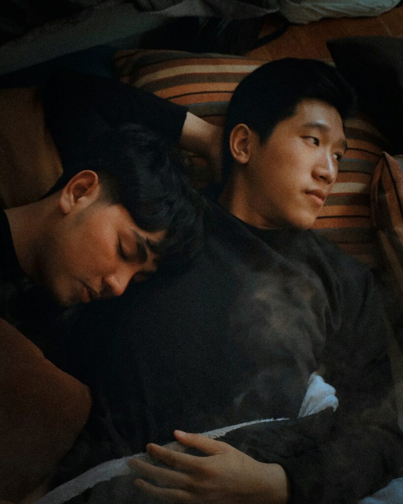 male couple in bed with one man looking off into distance