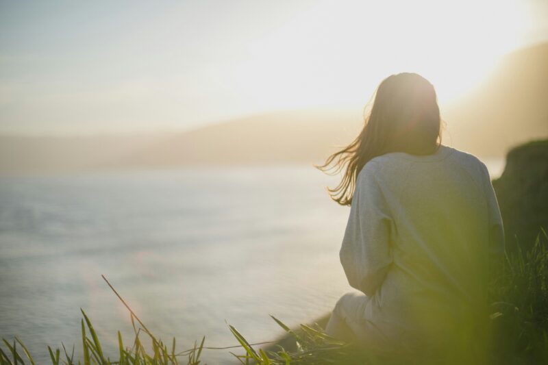girl sitting on cliff at sunset looking at the water