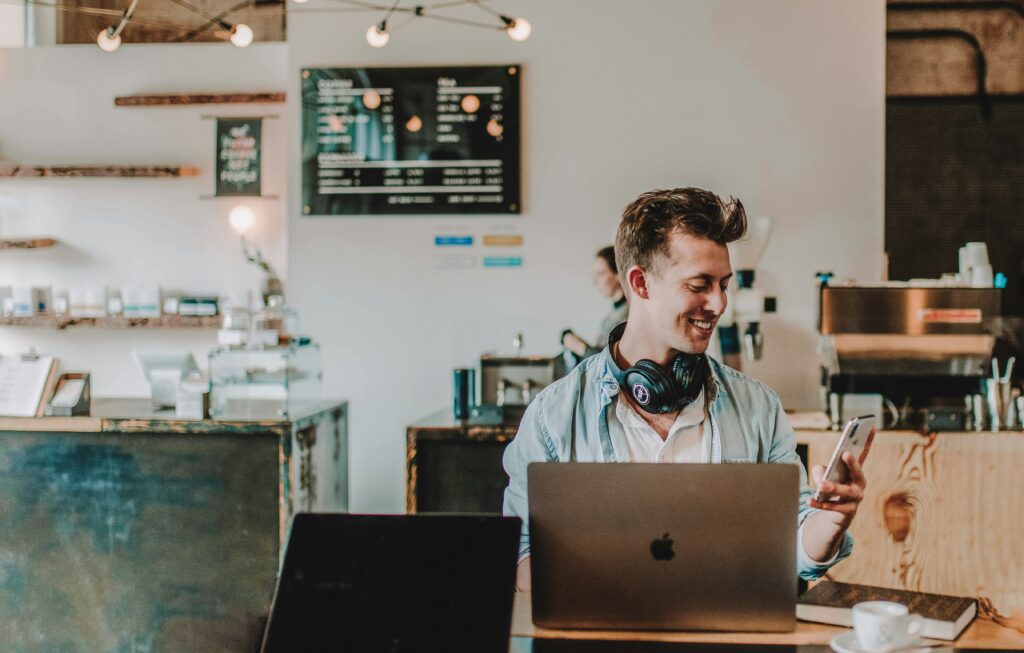 Young professional white man in coffee shop on phone smiling and emailing a therapist