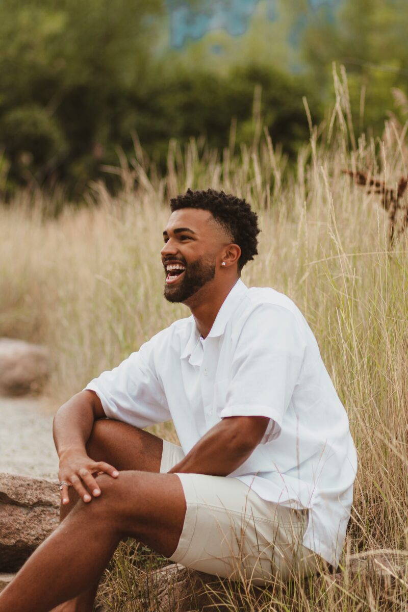 young black man smiling sitting in field with white shirt and khaki shorts