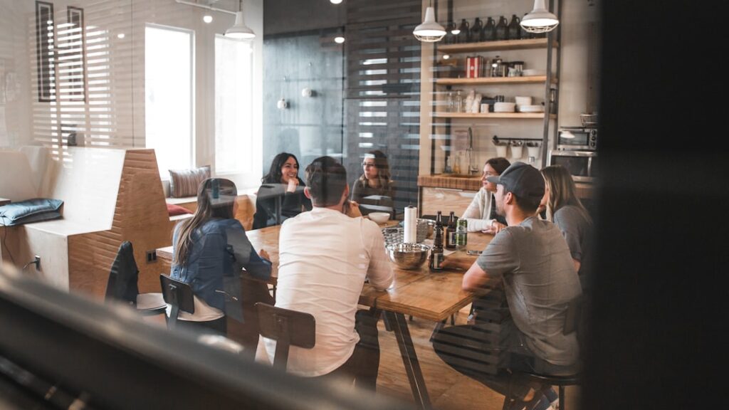 employees gathered in a glass meeting room around a brown table