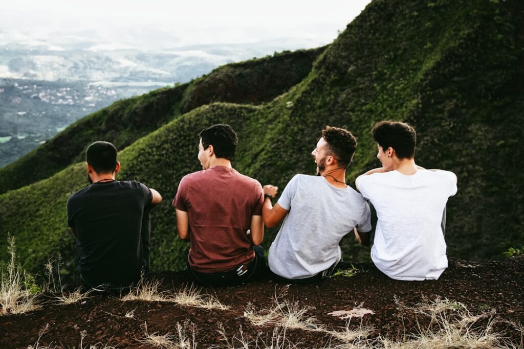 Four young adult men sitting on ledge laughing and staring at mountains in the distance