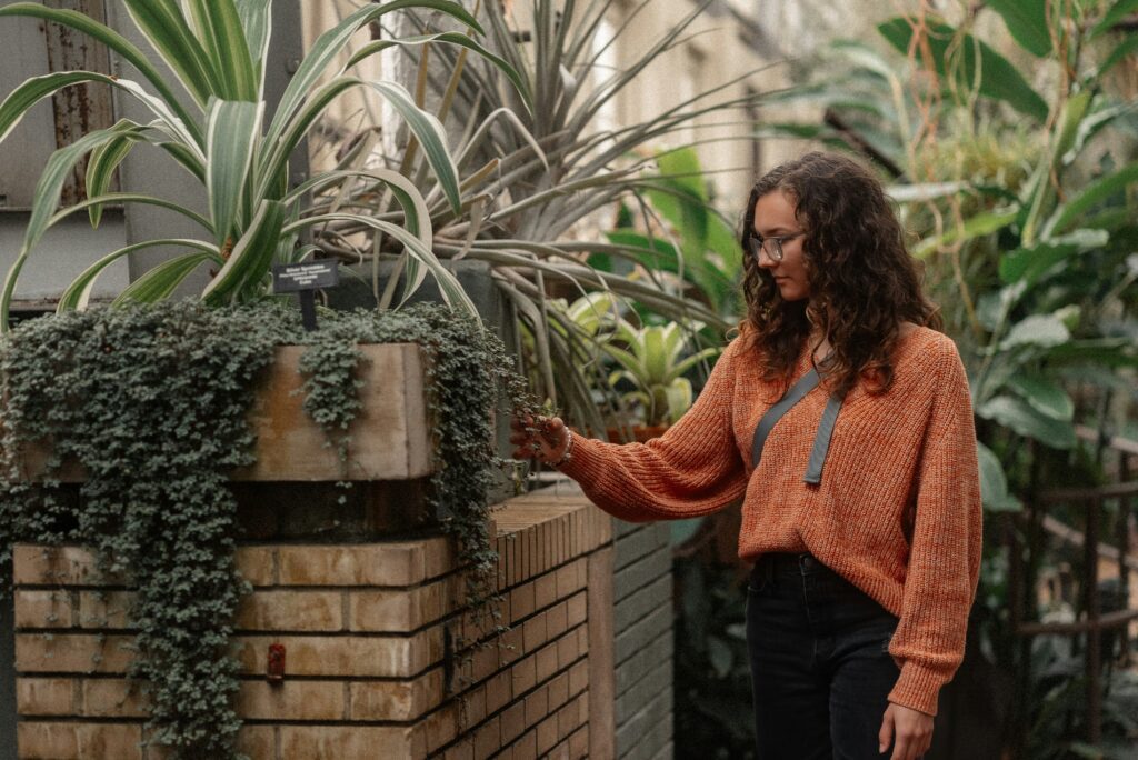 Woman in orange sweater walking through Garfield Park Conservatory looking at plants