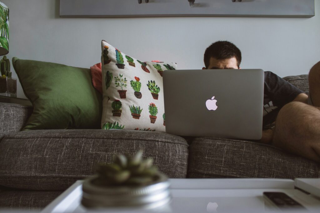 Man sitting on couch with his face hidden looking at computer
