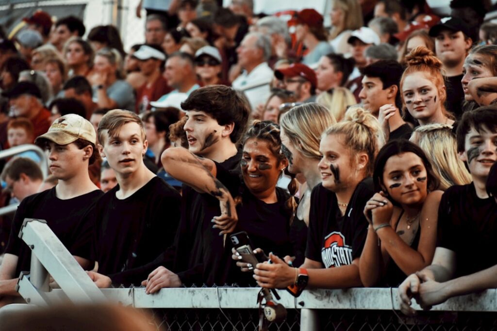 Modern teenagers dressed in black at high school football game in student section