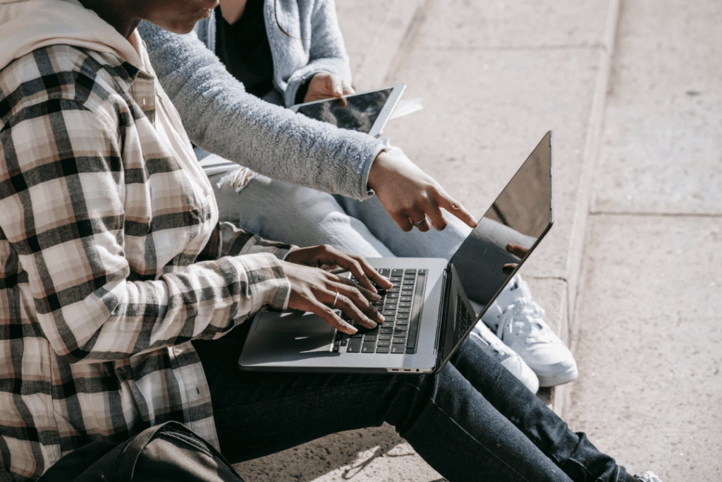 Young woman wearing a black and white plaid hoodie and another young woman with a great sweater looking over their research to find personal and professional support.