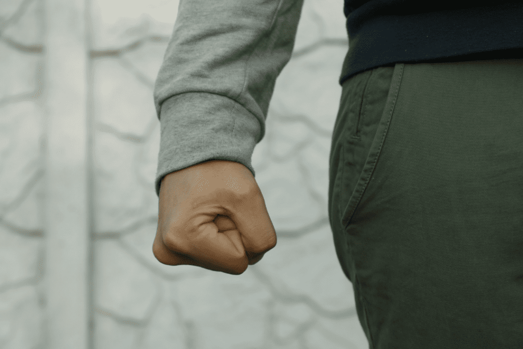 A young man wearing a grey and black sweater with his hand in a fist, representing negative emotions.