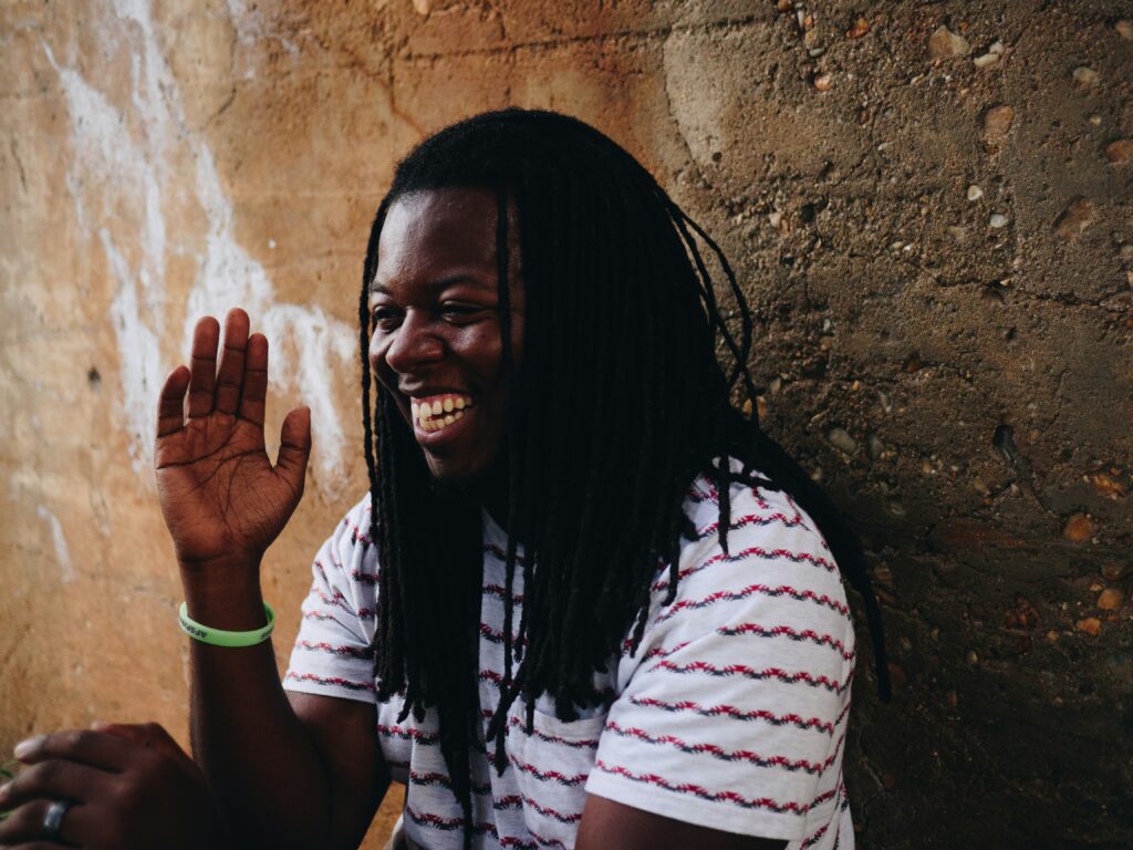 Black man with braids sitting in front of stone wall smiling because he doesn't have anxiety