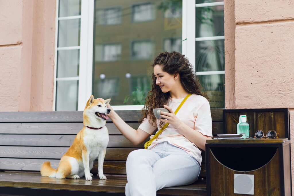Young woman smiling while sitting on bench drinking coffee and petting dog