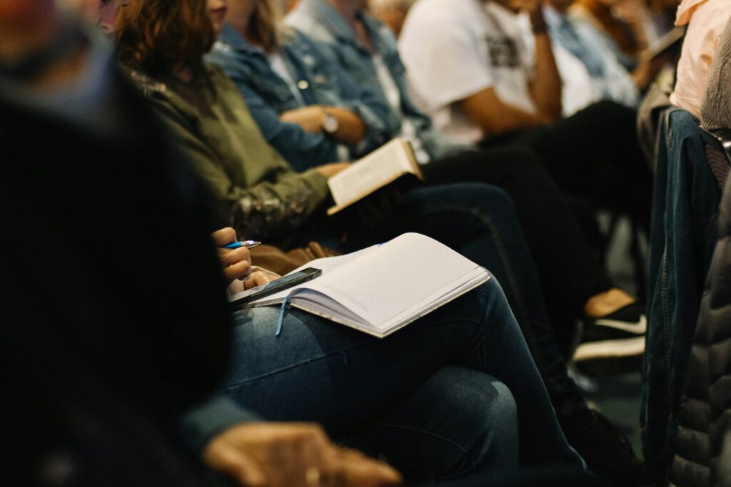 A group of people sitting in a church setting, some taking notes and holding Bibles—representing reflection, faith, and the complexities of religious experiences, including church hurt and spiritual healing.