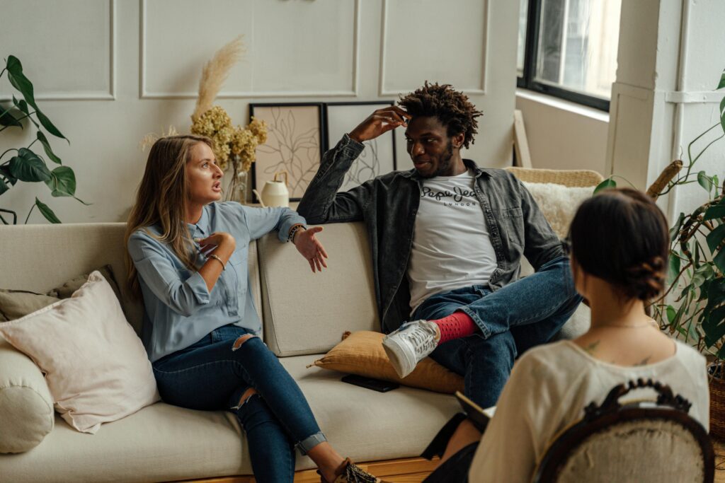 A couple in a therapy session, engaging in open and supportive conversation with a therapist about Sensate Focus exercises.