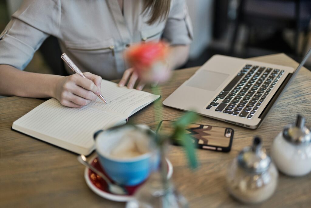 Person writing in a journal next to a laptop with coffee, planning personalized anxiety treatment goals in a calm workspace.