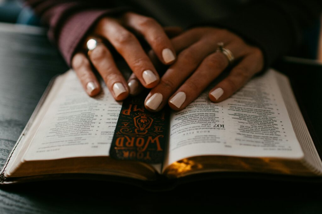 Hands resting on an open Bible with a bookmark, representing a moment of reflection, faith, and spiritual connection.