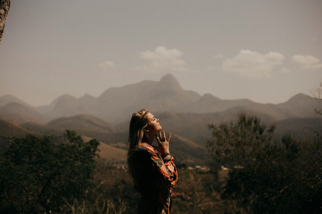 A woman standing in nature with her eyes closed and hands lifted, embracing peace, healing, and spiritual renewal.