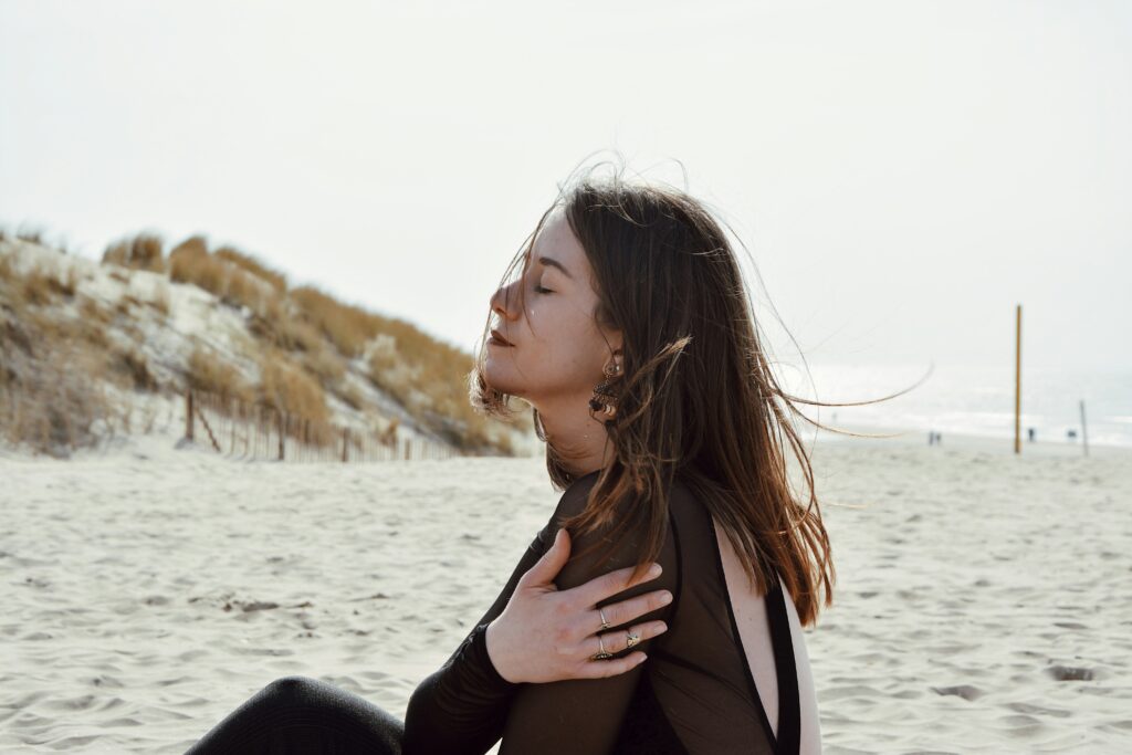 Woman practicing butterfly tapping on the beach with eyes closed, representing self-administered EMDR in a calming environment.