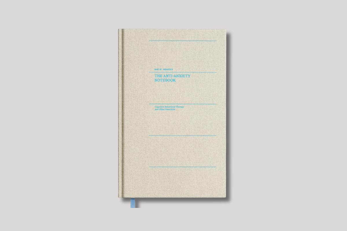 Hardcover "The Anti-Anxiety Notebook" with beige fabric cover and blue text, focused on Cognitive Behavioral Therapy.