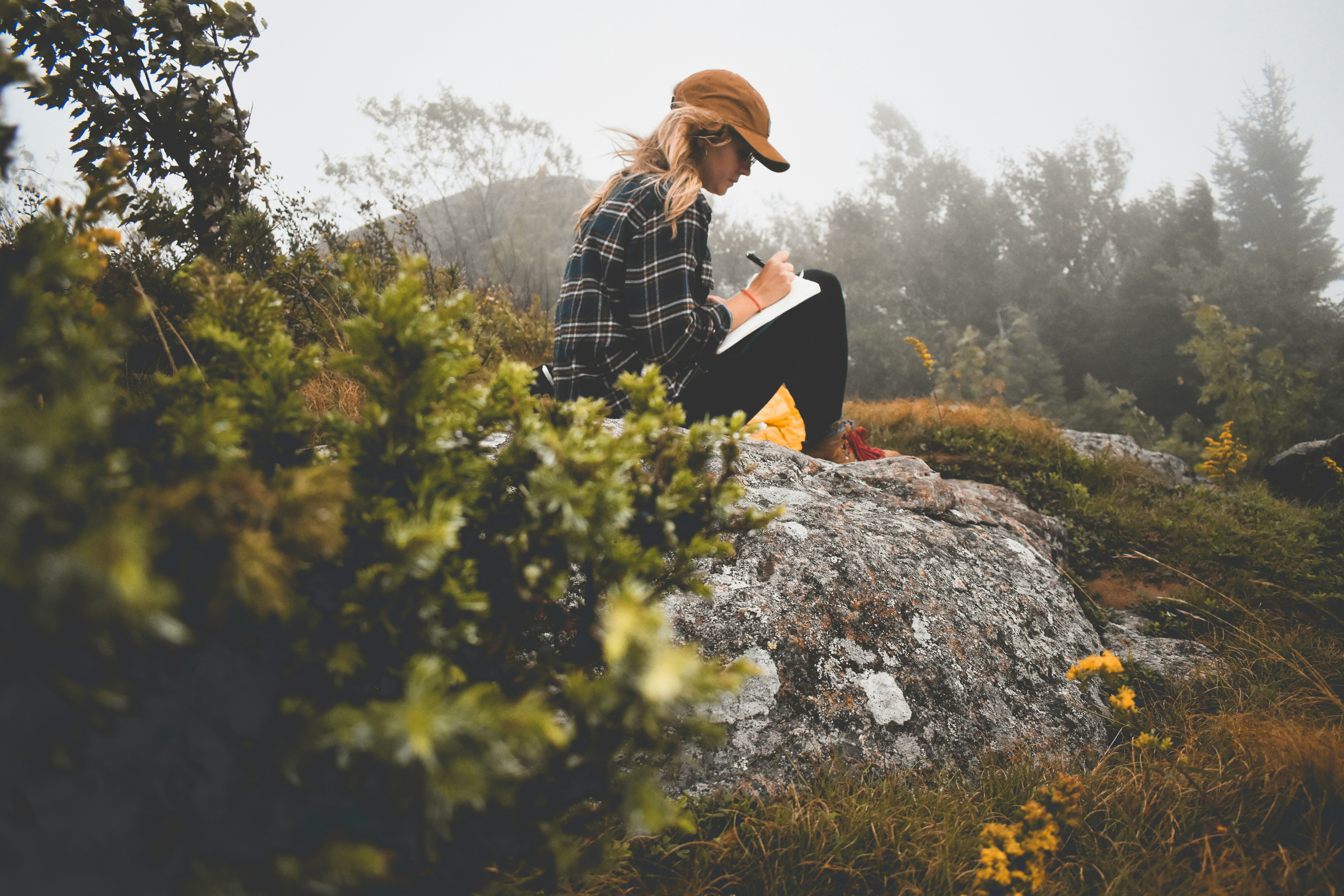 Woman journaling in a guided notebook while sitting on a rock in nature