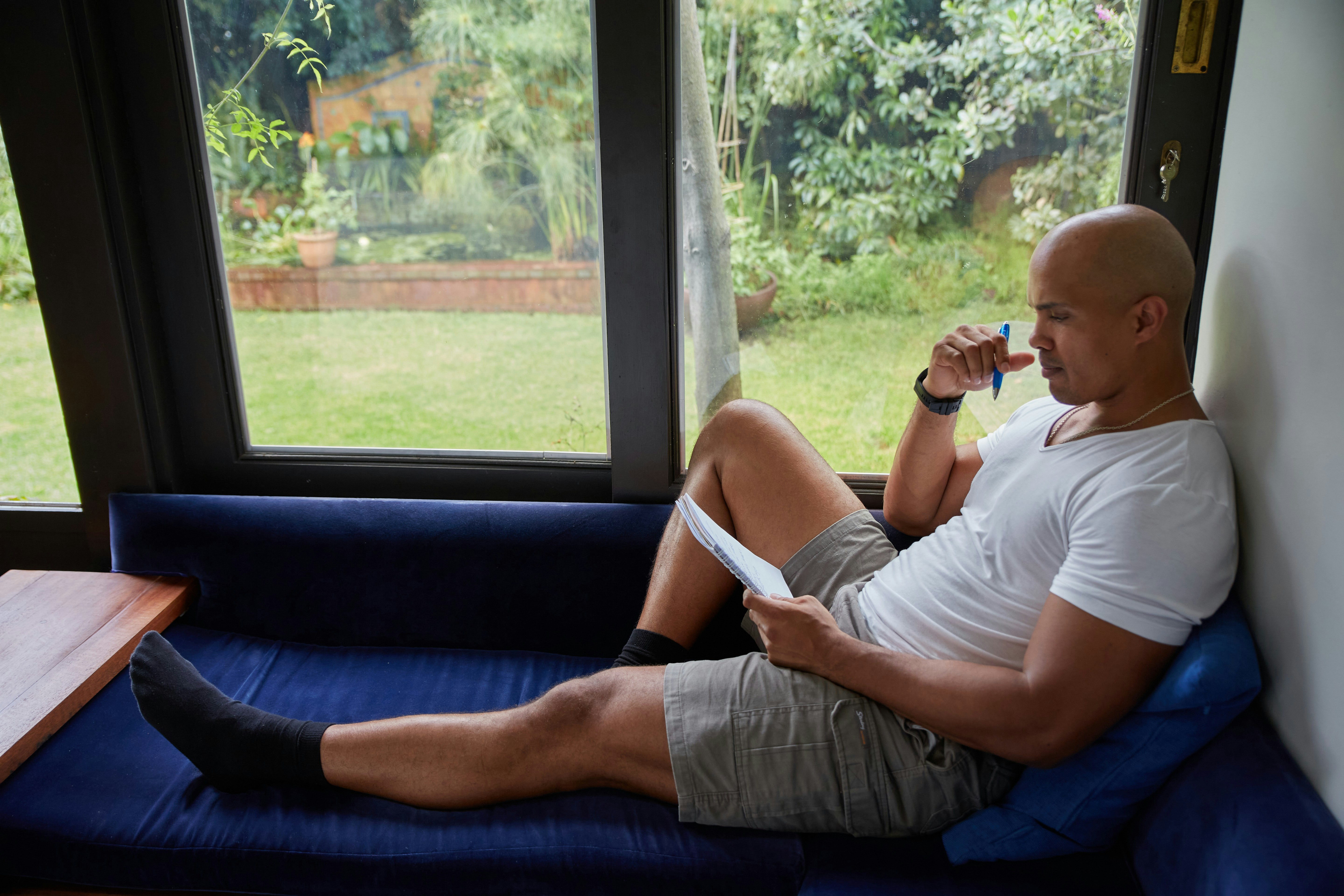 Man relaxing by a window seat while writing in a guided journal