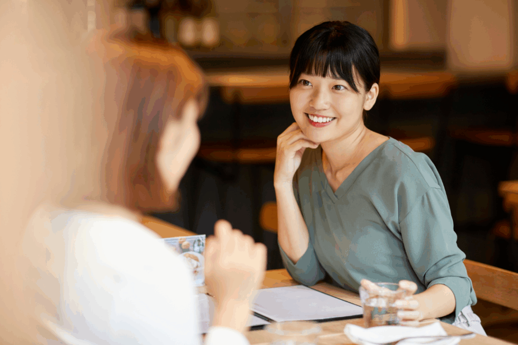 A woman leans in slightly as she speaks to another woman, her eyes searching and voice gentle, filled with a quiet vulnerability. There's a hopeful openness in her expression, as if she's reaching out for understanding, craving a genuine connection.