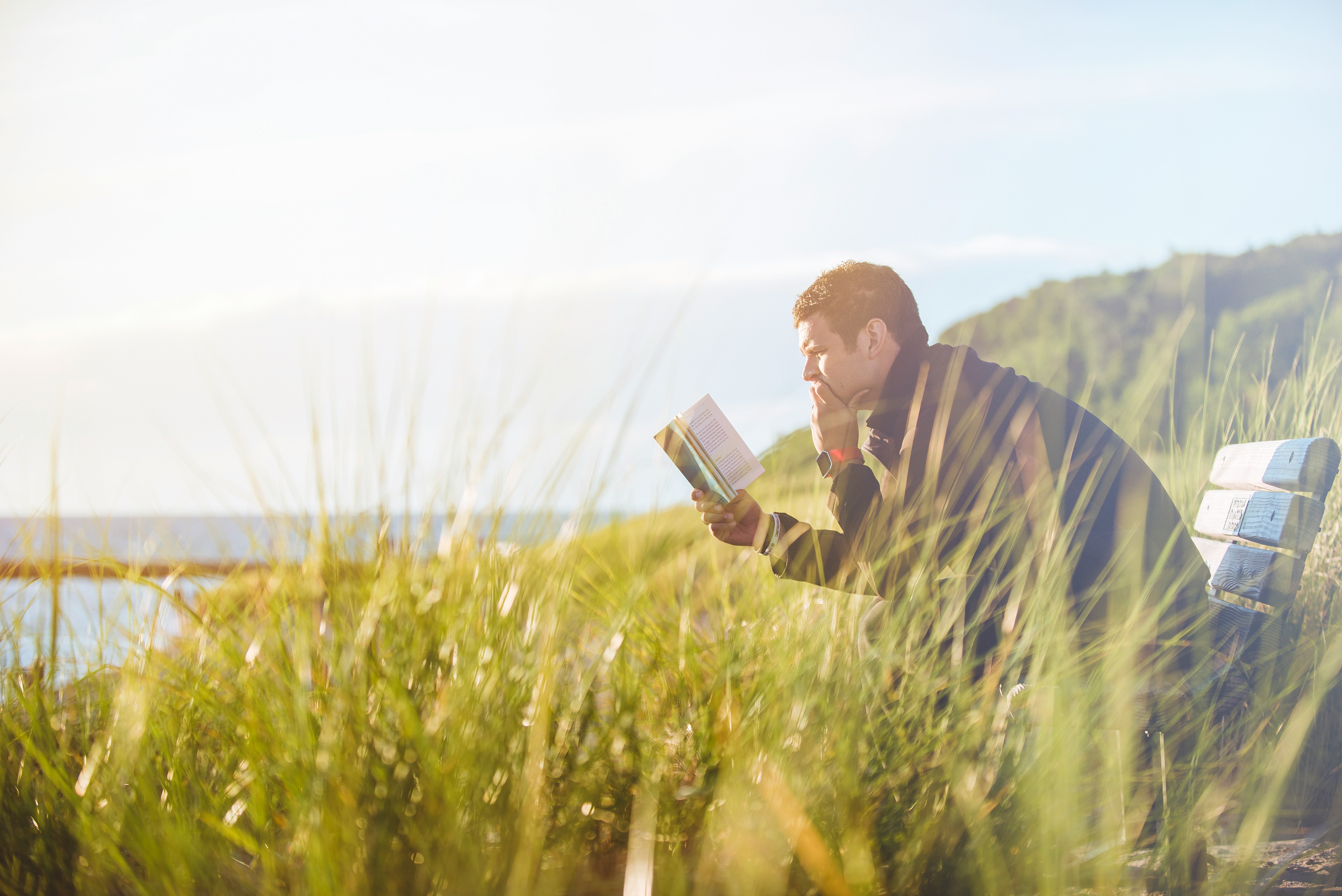 Man sitting on a bench in nature reading a book, symbolizing mindfulness and personal growth with an OCD workbook