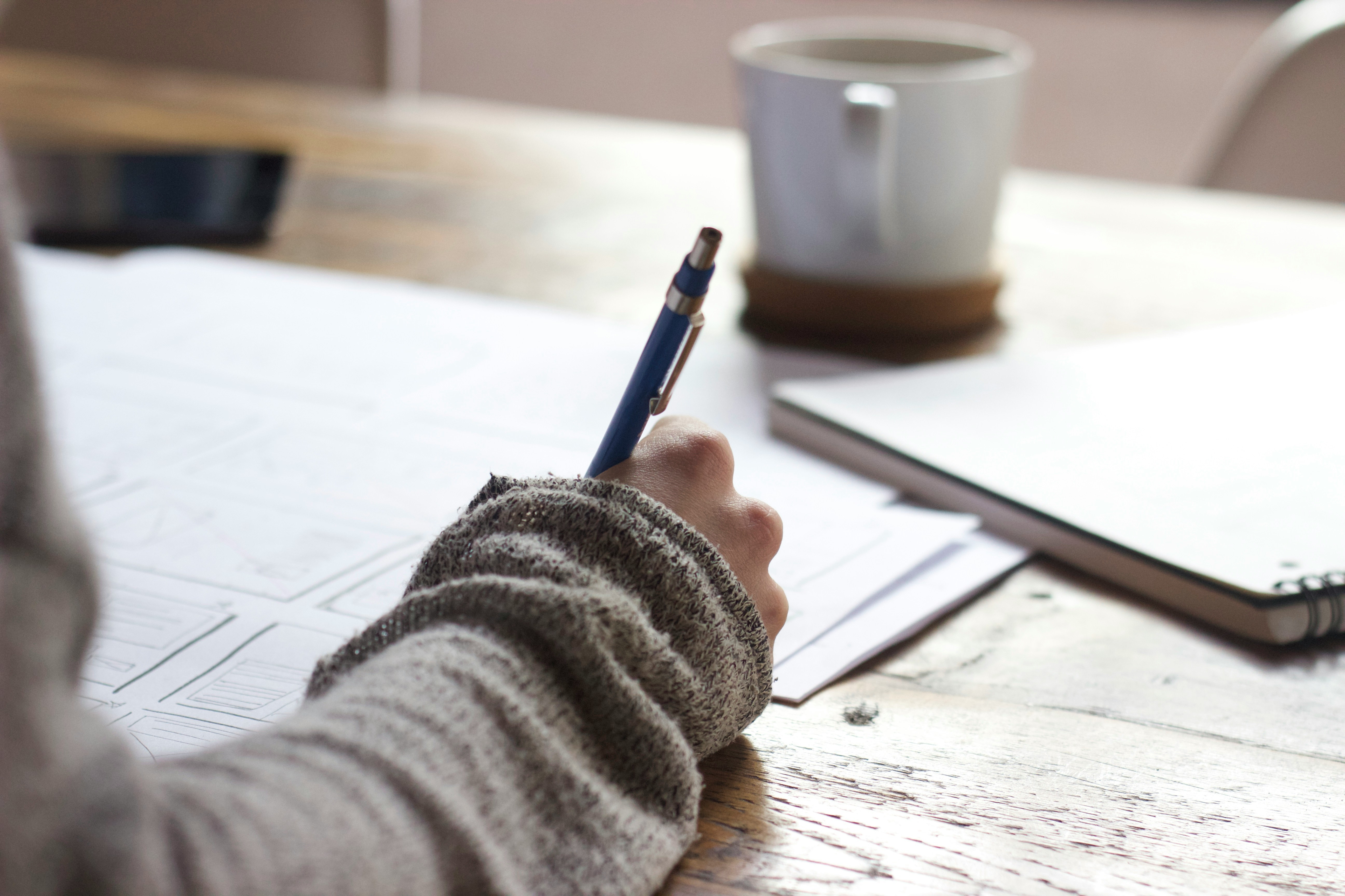 Person writing in a notebook with coffee on the table – studying with an OCD workbook