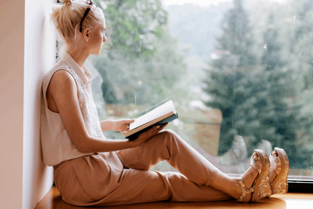 A picture of a girl, holding a book, staring outside in the window, feeling empty. 