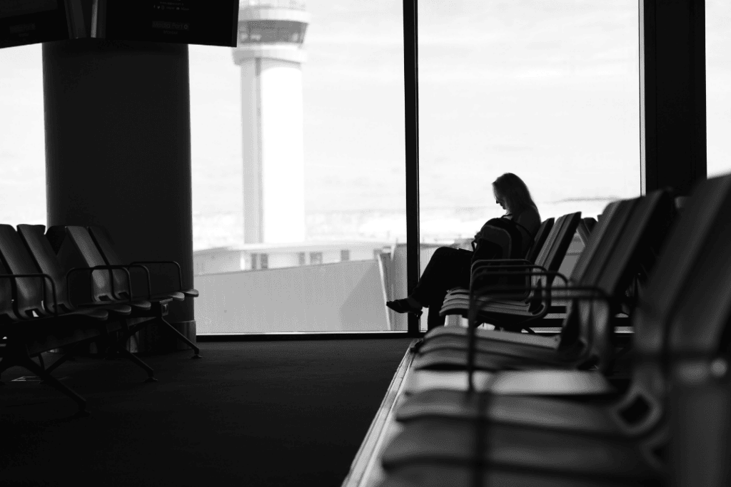 A black-and-white picture of a girl sitting in the lines of long empty chairs.