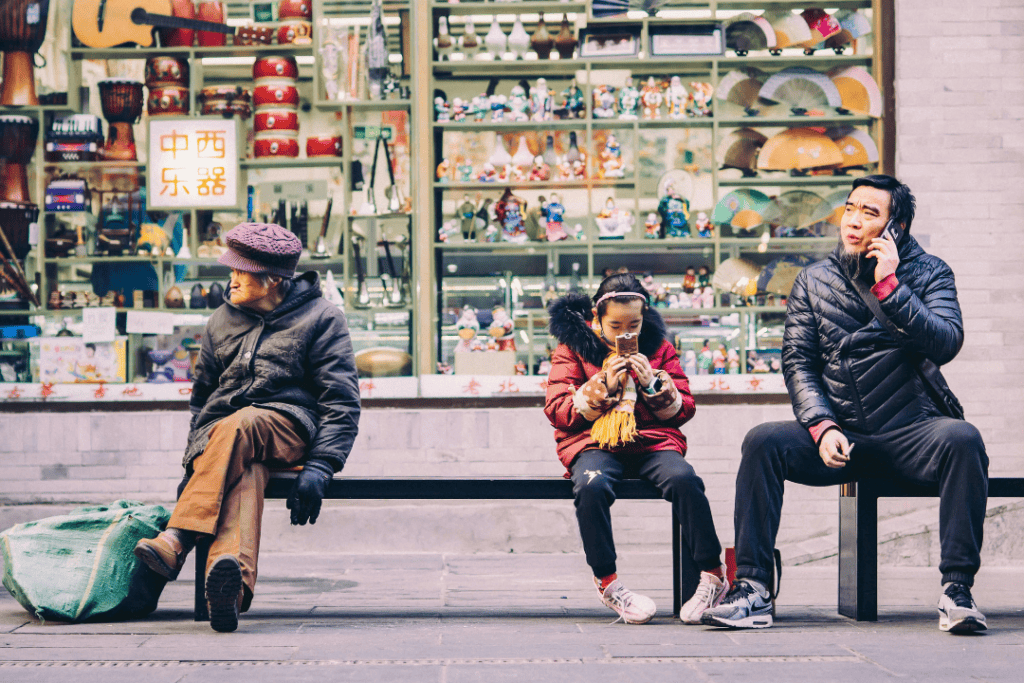 Three people sitting in a bench, representing different ages with different seasons of their life. The man on the right side was with his child, busy answering phone calls while his child is busy playing on her phone. The older woman on the other hand is just sitting, waiting for something, 